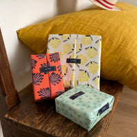 3 petits paquets cadeaux en coton réutilisables sur un banc en bois